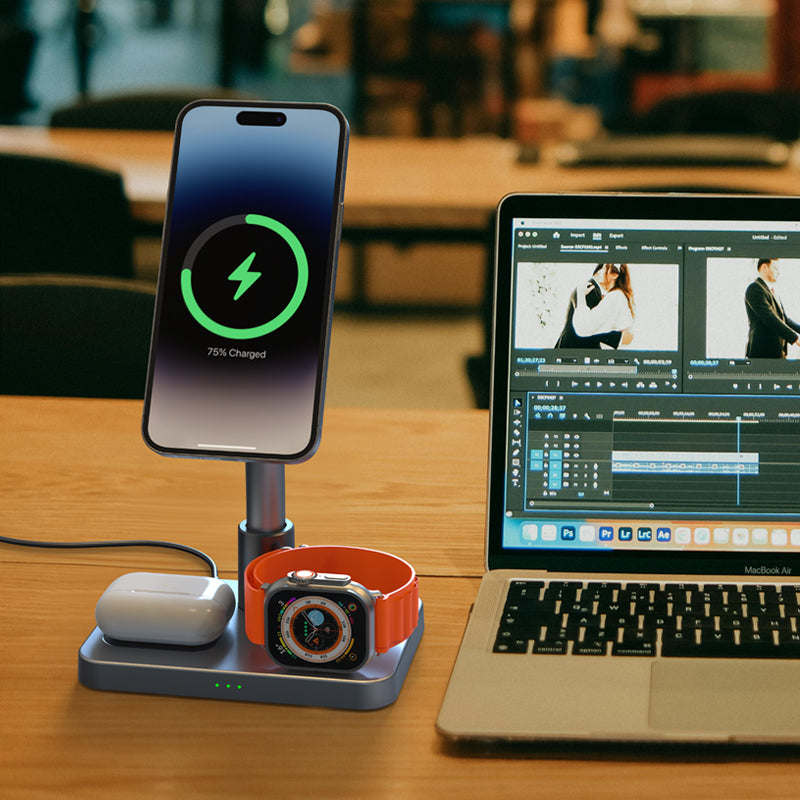 A desk with a charging station holding a smartphone, smartwatch, and earbuds next to an open laptop displaying a video editing program. The smartphone shows it's 75% charged.